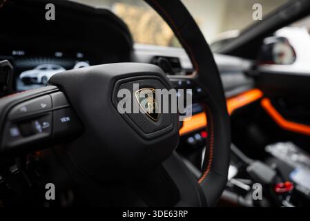 Vue rapprochée de l'intérieur d'une Lamborghini Urus se Orange dans un atelier. Volant avec écusson, surpiqûres et garnitures orange, tableau de bord numérique et Banque D'Images