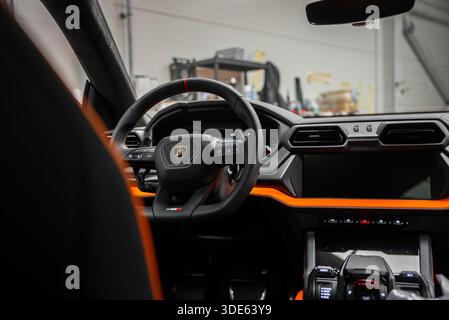 Vue intérieure rapprochée montrant la roue de l'écusson, le tableau de bord numérique, la garniture orange, les évents hexagonaux et les boutons-poussoirs dans un atelier, capturés avec une faible profondeur de f Banque D'Images