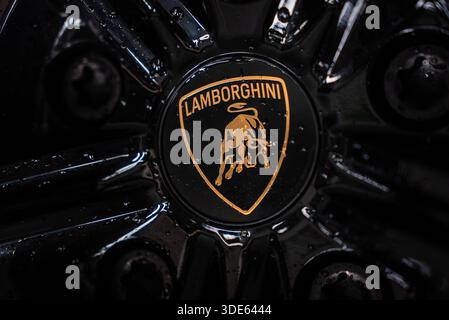 La vue rapprochée montre le taureau doré et le lettrage Lamborghini sur un enjoliveur de roue noir brillant avec des écrous de roue et des taches humides, suggérant un lavage récent sur un Orange Banque D'Images