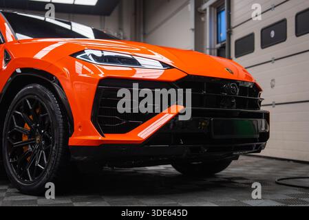 La vue en gros plan à angle bas montre l'avant gauche d'une Lamborghini Urus se orange dans une aire de service intérieure. Calandre noir brillant, phare à DEL, garnitures y, Banque D'Images