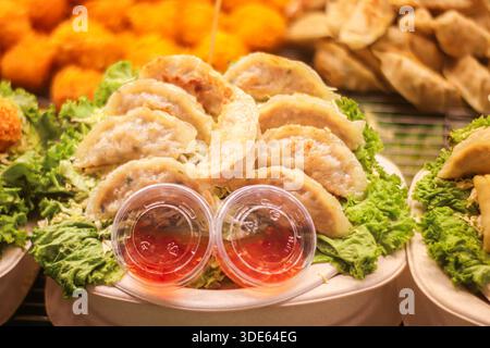 Cassez les boulettes gyoza avec sauce trempée sur laitue fraîche. Apéritif authentique du marché nocturne asiatique à usage éditorial et commercial. Banque D'Images