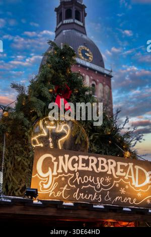Les boissons chaudes de Gingerbread House et d'autres stands brillent sous des guirlandes et un arc rouge, fixés par l'horloge et le dôme de la cathédrale de Riga dans la vieille ville de Riga, Lettonie à eveni Banque D'Images