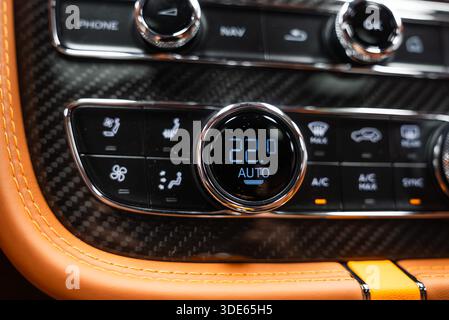 La vue intérieure en gros plan montre le panneau de commande de climatisation Bentley Bentayga Speed, la garniture en fibre de carbone, les coutures orange, les boutons chromés et le cadran numérique à 22,0 Banque D'Images