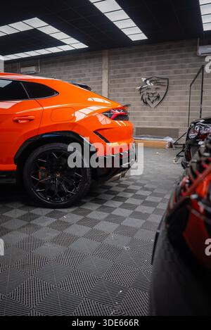 Vue rapprochée d'une Lamborghini Urus se orange montre une roue, un étrier orange et un feu arrière LED dans un atelier avec logo lion, plancher à damier et panneau Banque D'Images