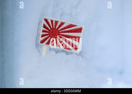 Drapeau du soleil levant du Japon dans un cadre enneigé. Symbolique de la culture historique, du tourisme hivernal et de l'identité nationale dans le froid. Banque D'Images