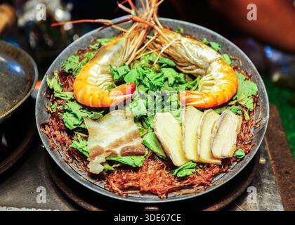 Vue de dessus de crevettes cuites à la vapeur avec vermicelles dans un pot thaïlandais traditionnel, mettant en valeur les fruits de mer authentiques maison et la culture chaleureuse de la cuisine familiale. Banque D'Images