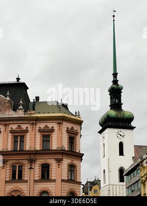 Brno, République tchèque - 29 novembre 2025 : un paysage urbain européen de Brno avec une architecture rose ornée à côté d'une église Saint-Jacques blanche et d'un g saisissant Banque D'Images