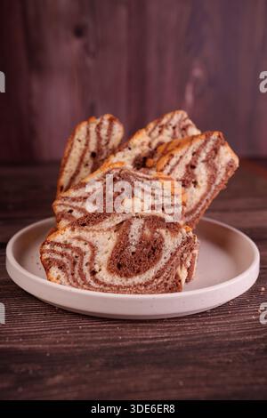 tranches de gâteau en marbre au chocolat et à la vanille artistiques disposées sur une assiette blanche avec un fond en bois rustique, mettant en valeur les motifs de tourbillons complexes Banque D'Images