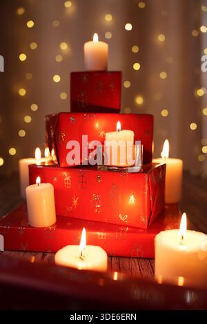 arrangement de vacances confortable avec des bougies scintillantes et des boîtes cadeaux rouges emballées de façon festive sur un fond doux et chaud de lumières de bokeh scintillantes, magie Banque D'Images