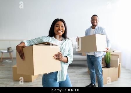 Un heureux couple afro-américain déménageant, tenant des boîtes en papier et les déballant après avoir déménagé dans son propre logement Banque D'Images