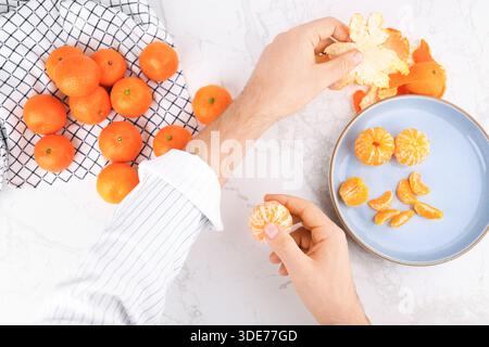 Mains masculines pelant des mandarines fraîches sur une table en marbre blanc. Vue de dessus de l'homme mangeant des agrumes sains. Photo de haute qualité Banque D'Images
