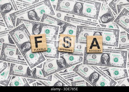 Les cubes en bois épellent FSA avec les mots flexible, dépense et compte sur eux. Les tuiles sont entourées d'une pile de billets d'un dollar américain. Concept de A. Banque D'Images