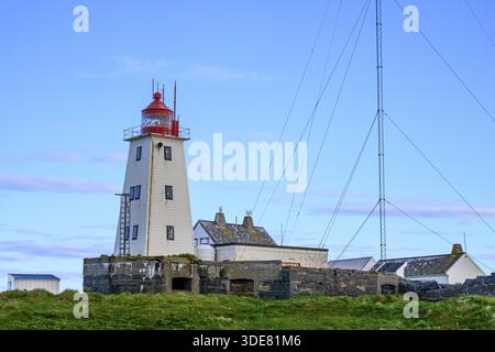 Phare blanc avec pointe rouge et antennes sur l'île ornithologique de Hornoya, entouré de collines herbeuses sous un ciel clair, Vardo, Finnmark, Norvège Banque D'Images