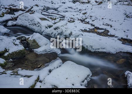 Un ruisseau coule à travers une zone de neige. Quelques pierres sont visibles et l'eau semble claire et fraîche. La région environnante est hivernale et calme. Perlba Banque D'Images
