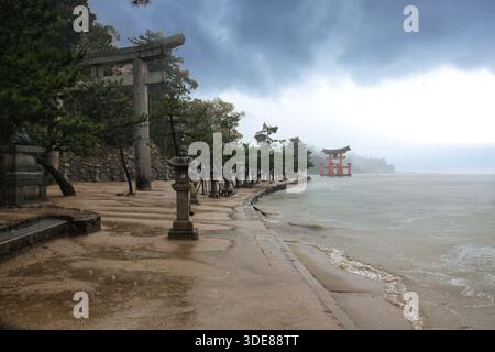 Itsukushima (Miyajima), Japon, 07/04/2016 Description : anciennes lanternes en pierre et Grande porte Torii à Miyajima sous le ciel orageux. Banque D'Images