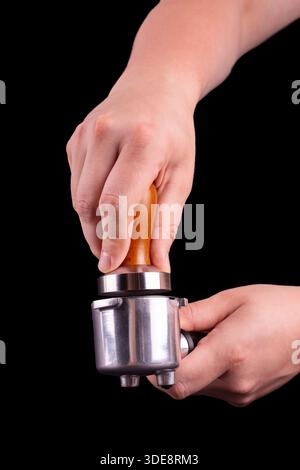 L'homme utilise un tamper pour presser le café du matin fraîchement moulu dans une tablette de café sur fond noir isolé Banque D'Images