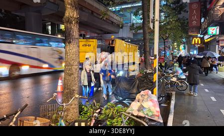 Taipei, Taïwan - 06 janvier 2026 collecte des ordures municipales la nuit montrant les travailleurs charger des sacs poubelles dans un camion d'assainissement sur une rue humide avec Banque D'Images