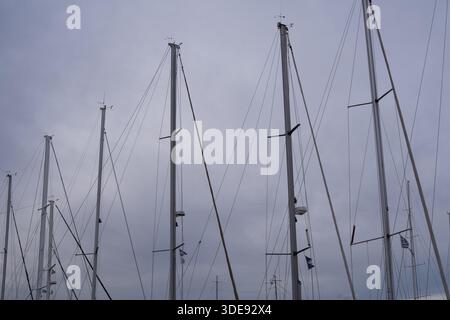 Mâts de voilier et gréement dans la marina sous ciel nuageux. Équipement nautique et fond maritime minimal. Banque D'Images