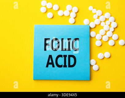 Symbole d'acide folique. Mot concept acide folique sur note bleue. Beau fond jaune avec des pilules. Médecine et concept d'acide folique. Copier l'espace Banque D'Images