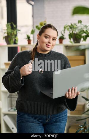 Un jeune manager de grande taille travaille en toute confiance sur son ordinateur portable dans un bureau élégant rempli de plantes. Banque D'Images
