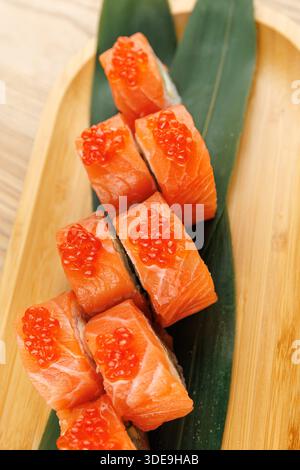 Les morceaux de sushi au saumon surmontés d'œufs d'orange vif sont soigneusement disposés sur une feuille verte placée sur un plateau en bois, mettant en valeur un présentati de nourriture vibrante Banque D'Images