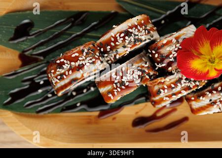 Les rouleaux de sushi sont disposés magnifiquement sur un plateau de bambou. Ils sont garnis de graines de sésame et arrosés de sauce. Une fleur ajoute de la couleur au pré Banque D'Images