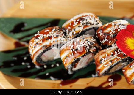 Des rouleaux de sushi recouverts de sauce anguille et saupoudrés de graines de sésame sont servis sur une feuille. Ce plat met en valeur des éléments de la cuisine japonaise dans un restaur Banque D'Images