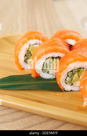 Des rouleaux de sushi fraîchement préparés remplis d'avocat et de légumes sont soigneusement disposés sur une assiette en bois, mettant en valeur des couleurs vives. Ce plat est prêt à en Banque D'Images