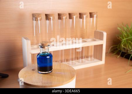 Six tubes à essai transparents sont disposés sur un portoir en bois. Au premier plan, une petite bouteille contenant du liquide bleu repose sur un couvercle rond en bois. La configuration est courante dans les laboratoires de chimie. Banque D'Images