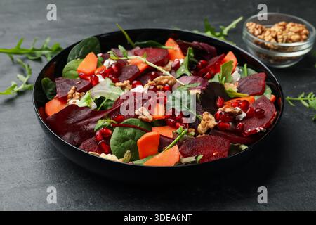 Délicieuse salade avec betterave, épinards, roquette, fromage, noix, graines de carotte et de grenade sur table noire, gros plan Banque D'Images