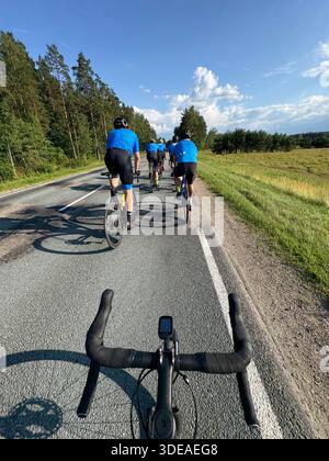 Cyclistes chevauchant à travers la campagne pittoresque sur une route pavée, vu du guidon sous le ciel bleu Banque D'Images