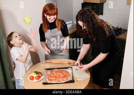 Soirée pizza familiale, s'amuser dans la cuisine, préparer les ingrédients pour la cuisson. Mère et fille créent et apprécient ensemble de délicieuses pizzas faites à la main. Une fille jongle avec le chou Banque D'Images
