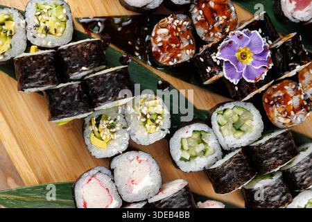 Les rouleaux de sushi sont agencés avec art sur une planche de bois. Des textures et des couleurs de différents types sont mises en évidence, mettant en valeur le savoir-faire culinaire. Banque D'Images