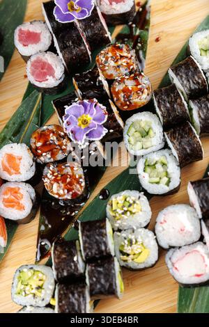 Une variété de rouleaux de sushi sont disposés sur un plateau de bambou. Les rouleaux comportent différentes garnitures telles que le poisson et les légumes. La sauce soja est présente, ajouter Banque D'Images