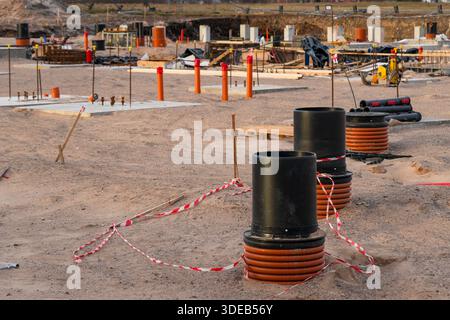 Chantier de construction de fondations avec sorties de tuyaux de communication souterrains, trous d'homme en plastique et puits utilitaires dans le sable avant l'installation de dalles de béton Banque D'Images