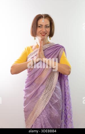 Une femme d'âge moyen dans un sari indien traditionnel plie ses bras en saluant Banque D'Images