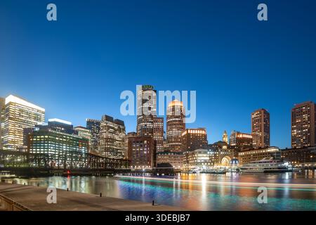 Une vue imprenable sur les gratte-ciel du centre-ville de Boston la nuit avec des gratte-ciel illuminés et des reflets dorés sur l'eau. Banque D'Images