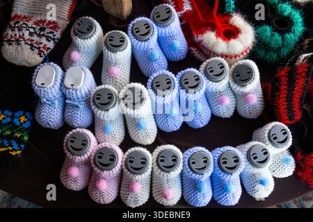 Chaussons tricotés à la main avec accessoires en plastique aux visages souriants. Adorables produits faits main en bleu, rose et blanc. Banque D'Images