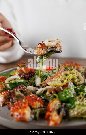 Une personne tient une fourchette avec un morceau de salade de fruits de mer, avec des légumes verts et des fruits de mer. Le cadre se sent détendu pendant qu'ils savourent le repas. Banque D'Images