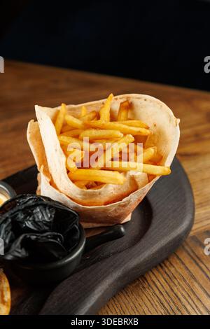 Les frites croustillantes sont placées dans un panier à tortilla, accompagnées d'un petit bol de sauce épaisse sur un plateau de service en bois. Ce plat est parfait pour Banque D'Images