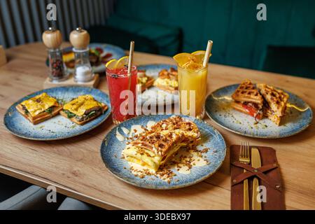 Des assiettes remplies de produits alimentaires colorés présentent une variété de plats de brunch et de boissons. Des gaufres fraîches, des sandwichs et des boissons aux fruits invitent les clients Banque D'Images