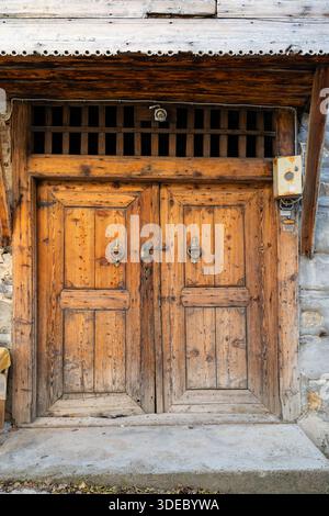 Une porte traditionnelle en bois à deux battants d'une maison historique en pierre, ornée de motifs martelés et sculptés à la main en grain de riz. Banque D'Images