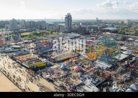 Vue aérienne du parc d'attractions animé de Coney Island, avec ses célèbres montagnes russes Wonder Wheel et Cyclone contrastant avec la lointaine ville Banque D'Images