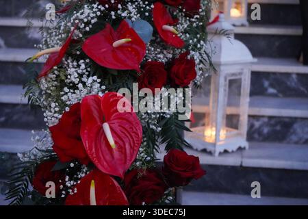 Décor romantique dans l'allée de mariage, avec roses rouges luxuriantes, anthuriums et lanternes blanches sur des escaliers en marbre. Banque D'Images