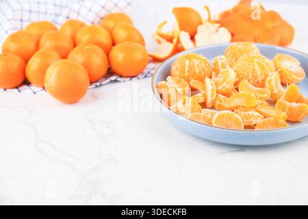 Segments de mandarine pelés sur une assiette bleue et mandarines entières fraîches sur une table en marbre blanc avec espace de copie. Photo de haute qualité Banque D'Images