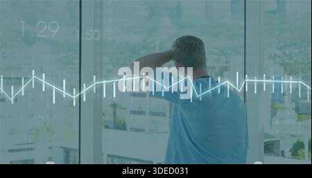 Homme debout dans des gommages médicaux bleu clair regardant par la fenêtre de l'hôpital, avec superposition des courbes ECG Banque D'Images