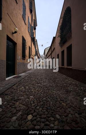 Étroite ruelle pavée avec des façades de bâtiments bas à l'ombre sur une journée nuageuse dans une ville italienne Banque D'Images