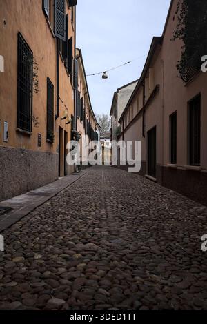 Étroite ruelle pavée avec des façades de bâtiments bas à l'ombre sur une journée nuageuse dans une ville italienne Banque D'Images