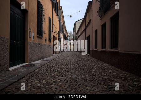 Étroite ruelle pavée avec des façades de bâtiments bas à l'ombre sur une journée nuageuse dans une ville italienne Banque D'Images