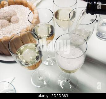 L'image montre une célébration ou un rassemblement social avec des verres de champagne mousseux versés dans des verres et un gâteau charlotte ou tiramisu. Banque D'Images